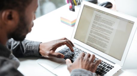 Cropped photo of serious young man sitting in office coworking. Looking aside using laptop computer. Focus on computer.